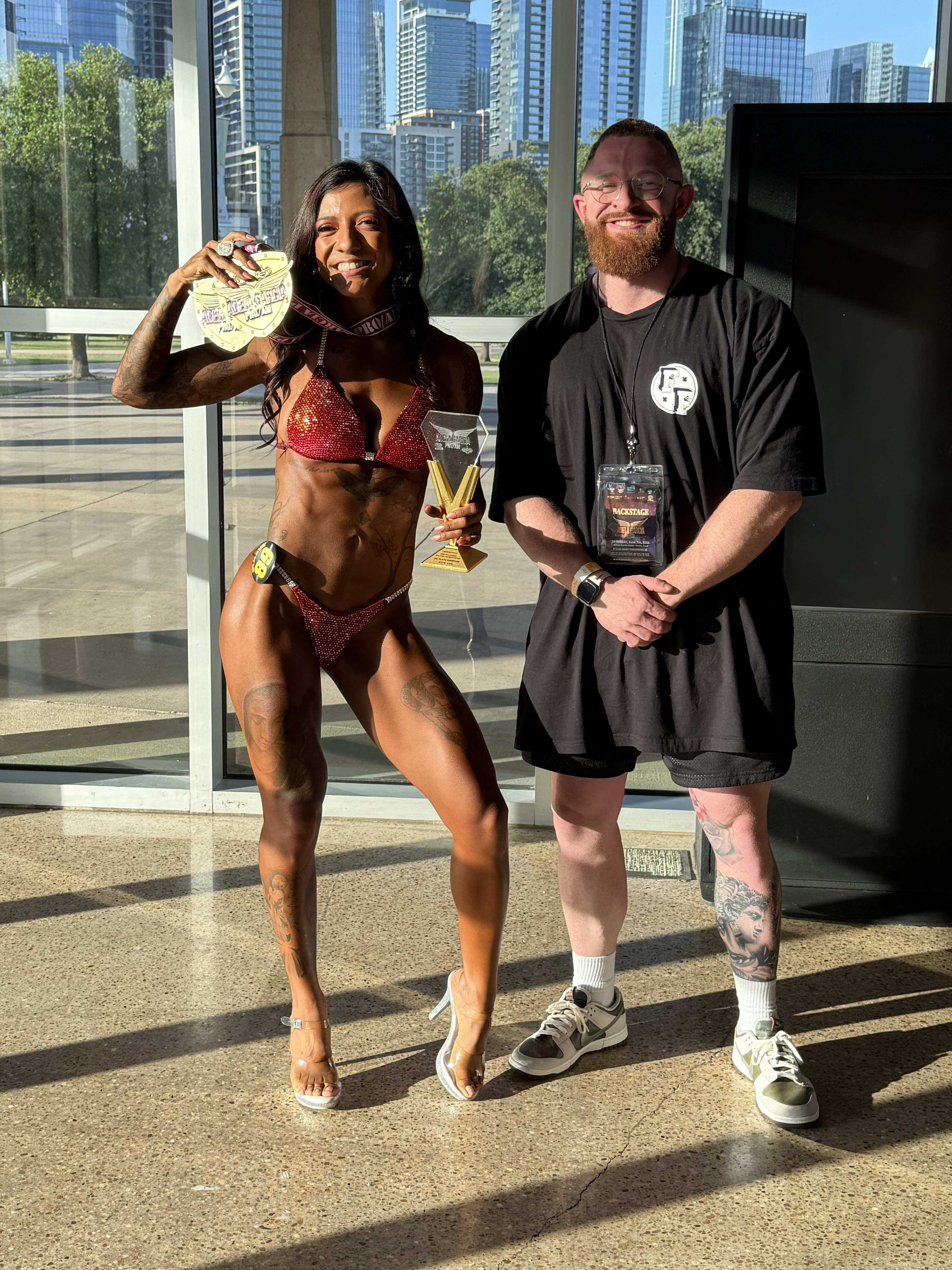 Personal Trainer Marlin Foy stands by a client competing at a bodybuilding competition
