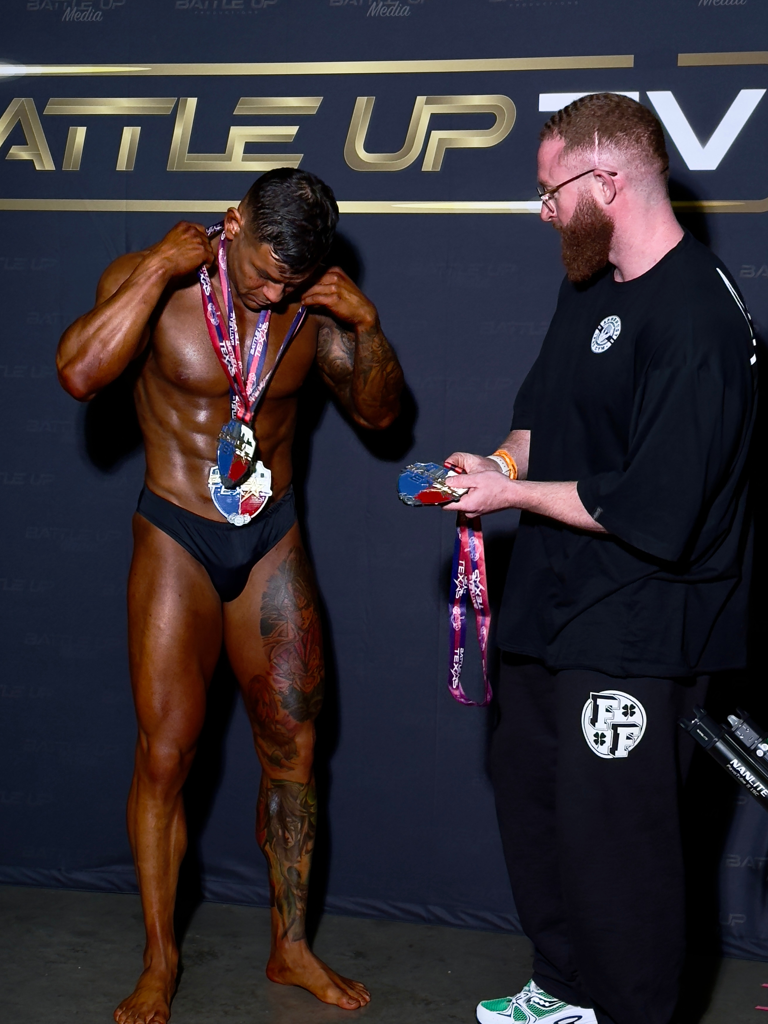 Personal Trainer Marlin Foy stands by a client competing at a bodybuilding competition